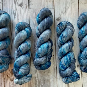 Puede incluir: Cinco ovillos de hilo en una combinación de colores azul y gris. El hilo está teñido a mano y tiene un aspecto moteado.
