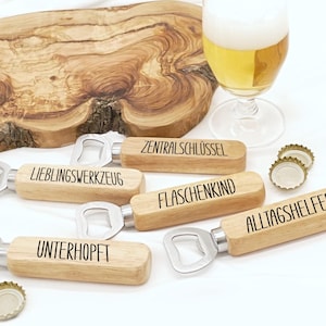 Könnte beinhalten: Holz-Flaschenöffner mit Edelstahlköpfen, jeweils mit einem deutschen Wort graviert. Die Öffner sind in der Nähe eines Bierglases und eines Holzbretts angeordnet. In der Nähe liegen Kronkorken.