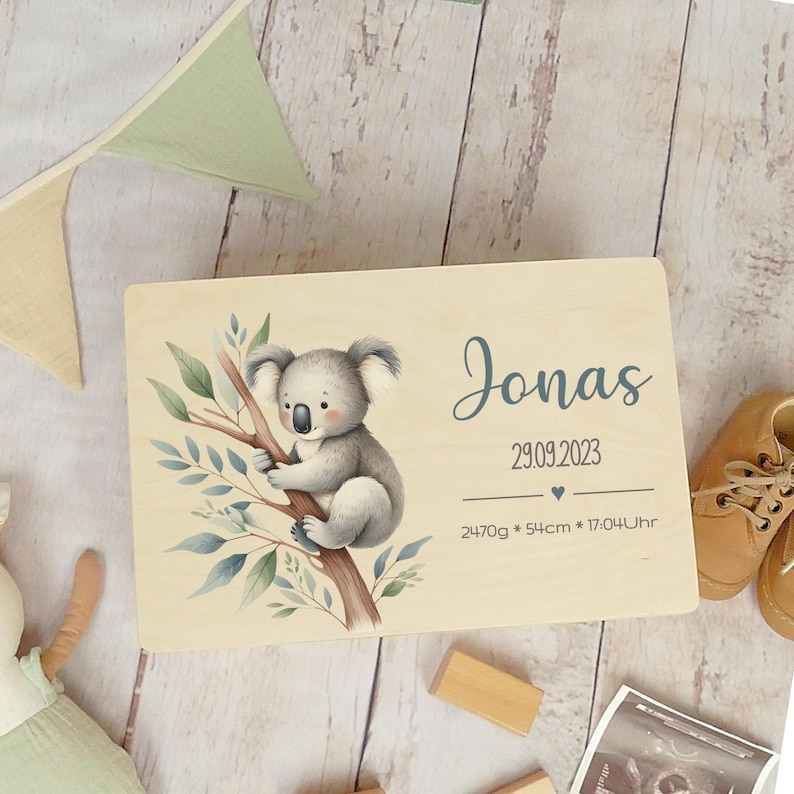 May include: A wooden keepsake box with a koala illustration and the name Jonas, birthdate 29.09.2023, weight 2470g, length 54cm, and time 17:04 Uhr.