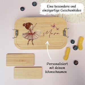 Pu&ograve; includere: Un portapranzo in legno chiaro con un'illustrazione di ballerina e il nome "Mara". La scatola ha chiusure in metallo e due piccoli pezzi rettangolari di legno. Il testo sulla scatola recita "Personalizzato con il tuo nome desiderato".
