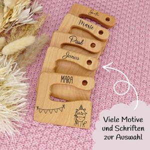 Könnte beinhalten: Fünf Holzschneidebretter mit gebogenen Griffen, jedes mit einem Namen graviert: Greta, Marie, Paul, Jonas und Mara. Das untere Brett zeigt eine Einhorn-Illustration und den Text "Viele Motive und Schriften zur Auswahl".