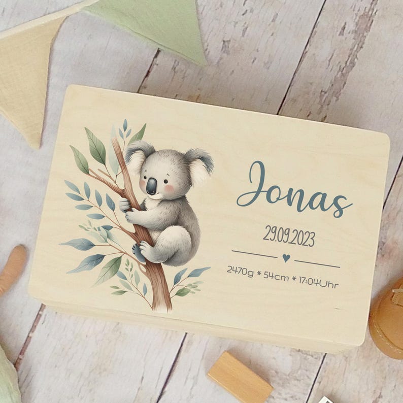 May include: A wooden keepsake box with a koala illustration and the name Jonas, the date 29.09.2023, and the text 2470g * 54cm * 17:04Uhr.