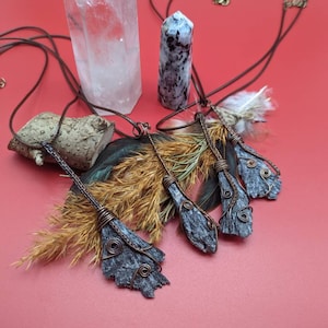 May include: Four gray and brown wire-wrapped pendants with feathers and a crystal point on a red background.