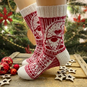Könnte beinhalten: Ein Paar weiße und rote Stricksocken mit einem weihnachtlichen Design. Die Socken haben ein weißes Schneeflockenmuster und ein rotes Weihnachtsmann-Gesicht.
