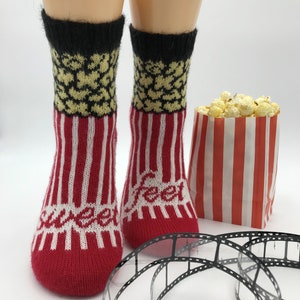 Könnte beinhalten: Rot-weiß gestreifte Socken mit einem Popcorn-Design oben. Die Socken liegen neben einem rot-weiß gestreiften Popcorn-Beutel und einer Filmrolle.