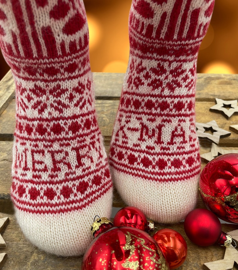 Op de afbeelding: Paar rood-witte gebreide sokken met een kerstpatroon. De sokken liggen op een houten oppervlak met rode en gouden ornamenten.