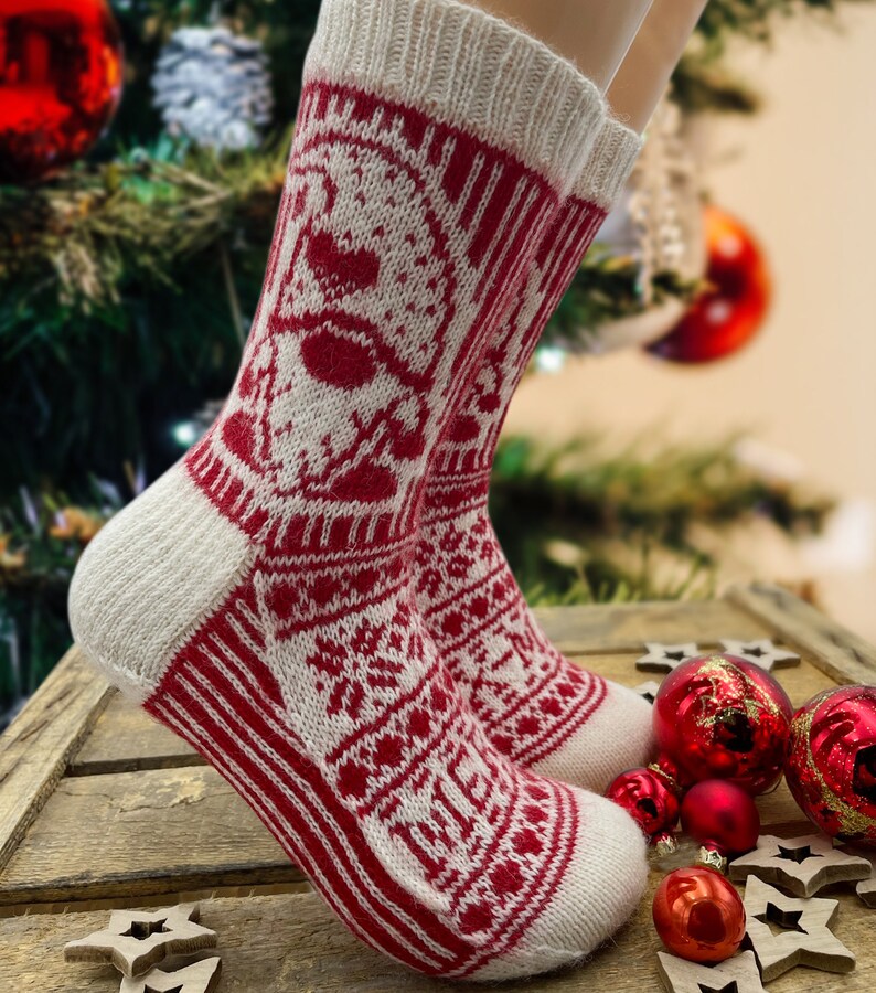 Op de afbeelding: Witte en rode gebreide sokken met een kerstthema. De sokken hebben een sneeuwvlok, een rendier en een kerstboom.