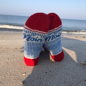 May include: A pair of red, white, and blue striped socks with the word "Peace" written on them. The socks are lying on a sandy beach.