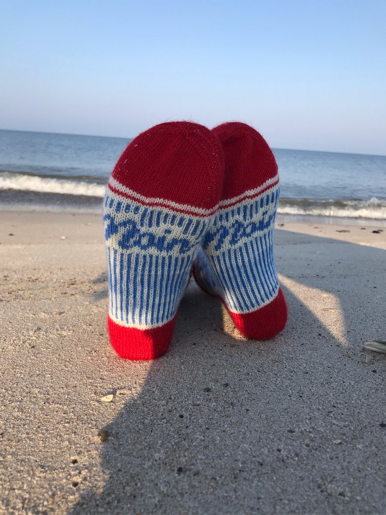 May include: A pair of red, white, and blue striped socks with the word "Peace" written on them. The socks are lying on a sandy beach.