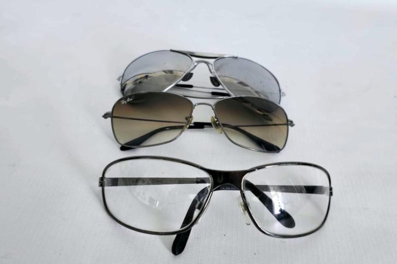 Puede incluir: Se muestran tres pares de gafas sobre un fondo blanco. El par superior son gafas de sol de aviador plateadas. El par del medio son gafas de sol degradadas marrones. El par inferior son gafas con montura negra y lentes transparentes.