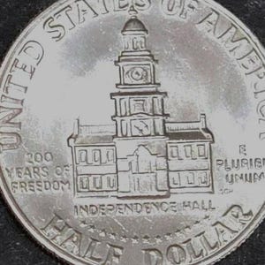 May include: A silver half dollar coin featuring Independence Hall. The coin is inscribed with "200 Years of Freedom" and "United States of America". The words "E Pluribus Unum" are also visible.