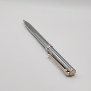 May include: A silver and gold ballpoint pen. The pen has a shiny silver barrel with gold accents at the tip, clip, and the band near the center. The pen is angled slightly to the right against a white background.