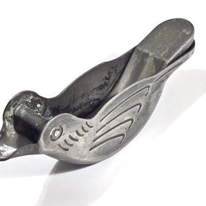 May include: A vintage metal bird-shaped nutcracker. The nutcracker is silver-colored with etched details, including wing and eye designs. The bird's beak is open, ready to crack nuts. The nutcracker is approximately 6 inches long.