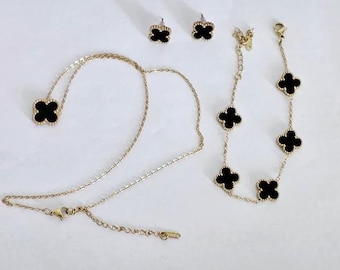May include: A gold-toned jewelry set featuring a necklace, bracelet, and earrings. Each piece has a clover-shaped black onyx design. The necklace and bracelet have multiple clovers, while the earrings and necklace pendant have one.