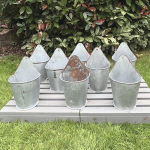 May include: A collection of eight galvanised metal wall planters with a conical back plate featuring a single mounting hole. Each bucket-shaped container has a weathered silver finish with visible rust spots and a tapered, open-top design.