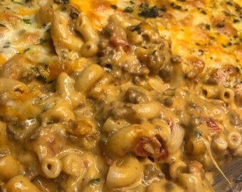 Puede incluir: Una fuente de horno llena de una mezcla cremosa de macarrones y carne de res con queso. La capa superior está cubierta de queso derretido y espolvoreada con hierbas.