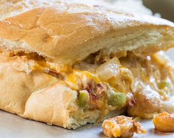Puede incluir: Primer plano de un sándwich de queso con un relleno cremoso, cebollas y pimientos verdes. El sándwich está cortado por la mitad y el relleno se está saliendo.