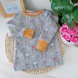 May include: A gray long-sleeved shirt with a deer print. The deer are pink and white with gold crowns. The shirt has mustard yellow cuffs.