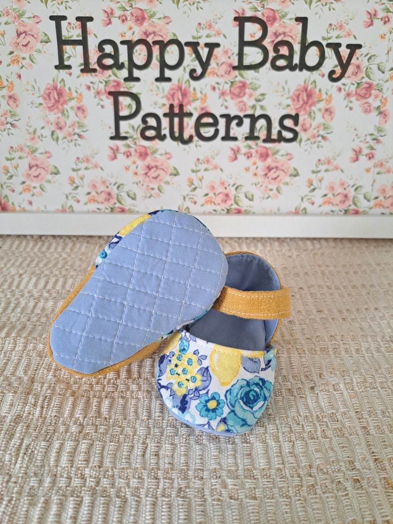 May include: Baby shoes with a floral pattern in blue and yellow, featuring a quilted light blue sole and a mustard yellow strap. The background includes the text "Happy Baby Patterns" over a floral design.