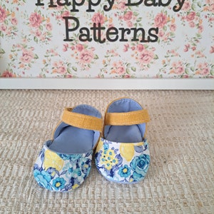 May include: A pair of baby shoes with a floral lemon pattern on the toe and a light blue interior. The shoes have a mustard yellow strap and are set against a floral background with the text "Happy Baby Patterns".