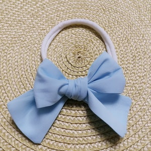 May include: A light blue fabric bow headband with a white elastic band.
