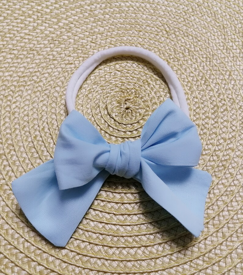 May include: A light blue fabric bow headband with a white elastic band.
