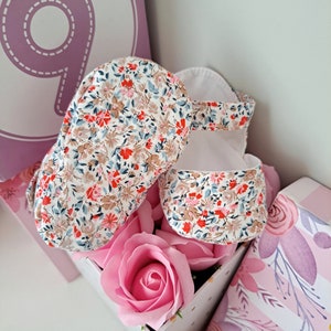 May include: Baby sandals with a floral pattern in red, blue, and brown on a white background. The sandals are placed in a decorative box with a pink rose. A large number 9 is visible in the background.