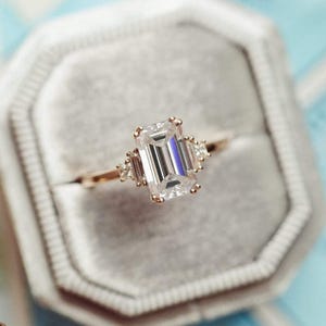 May include: A gold ring featuring an emerald-cut diamond with smaller diamonds on the band.