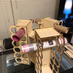 Pode incluir: Organizador de armazenamento artesanal de madeira com múltiplos compartimentos para guardar rolos de vinil, papel e outros materiais de artesanato. O organizador tem um acabamento em madeira clara e apresenta uma variedade de recortes circulaires.