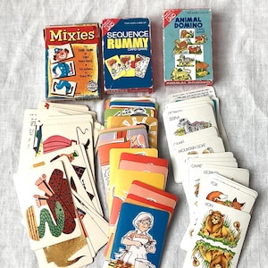 May include: A collection of vintage card games, including "Mixies," "Sequence Rummy," and "Animal Domino." The cards feature colorful illustrations of various characters and animals. The boxes are in various colors, including blue, red, and green.