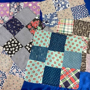 May include: A collection of fabric squares arranged in overlapping patchwork sections. The squares feature diverse patterns including floral prints, gingham checks, geometric shapes, plaids, and polka dots in various colors like blue, red, and purple.
