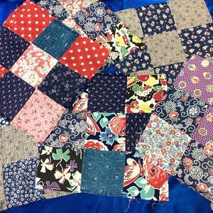 May include: A collection of square fabric patches arranged in a patchwork quilt style. The squares feature various patterns including red stars, blue floral prints, geometric grids, and multi-colored botanical designs in shades of red, blue, and white.