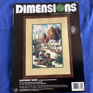 May include: A Dimensions counted cross stitch kit titled "Southwest Mesa" featuring a desert landscape with mountains, cacti, and pottery. The frame size is 10" x 15" without a mat, or 15" x 20" with a mat. Includes cotton embroidery thread and instructions.