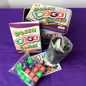 May include: A boxed game set titled "Dozen Dice Games" with a purple and white box and a metal tin. The set includes dice in red, green, and blue, and a black cup. The box reads "Shake, Rattle & Roll 12 Different Ways!"