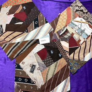 May include: Three diamond-shaped textile art pieces, each composed of repurposed neckties. The ties feature various patterns, including stripes, paisleys, and geometric designs, in shades of brown, beige, and burgundy. Some ties bear designer labels. The pieces are arranged on a purple surface.