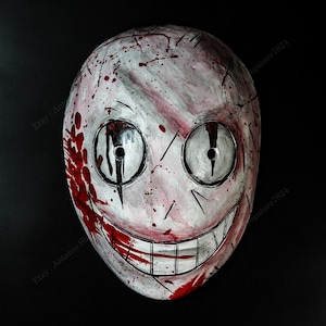 May include: A white mask with a stitched design and a sinister grin. The mask has large, round eye holes and is splattered with red paint, creating a horror-themed aesthetic.