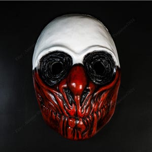 Op de afbeelding: Een volledig gezichtsmasker met een wit bovenstuk en een rood onderstuk. De oogkassen zijn zwart en de neus is rood. Het masker heeft een dreigende, skeletachtige uitstraling, met een gedetailleerd, getextureerd oppervlak.