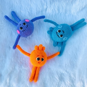May include: Three crocheted plush toys in the shape of octopus with smiling faces. The octopus are blue, orange, and light blue.