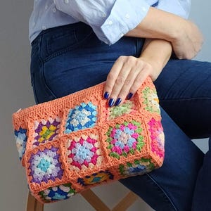 Crochet zipper clutch with peach border and multicolor granny-square panels; handmade crochet purse ideal as a makeup or toiletry bag.