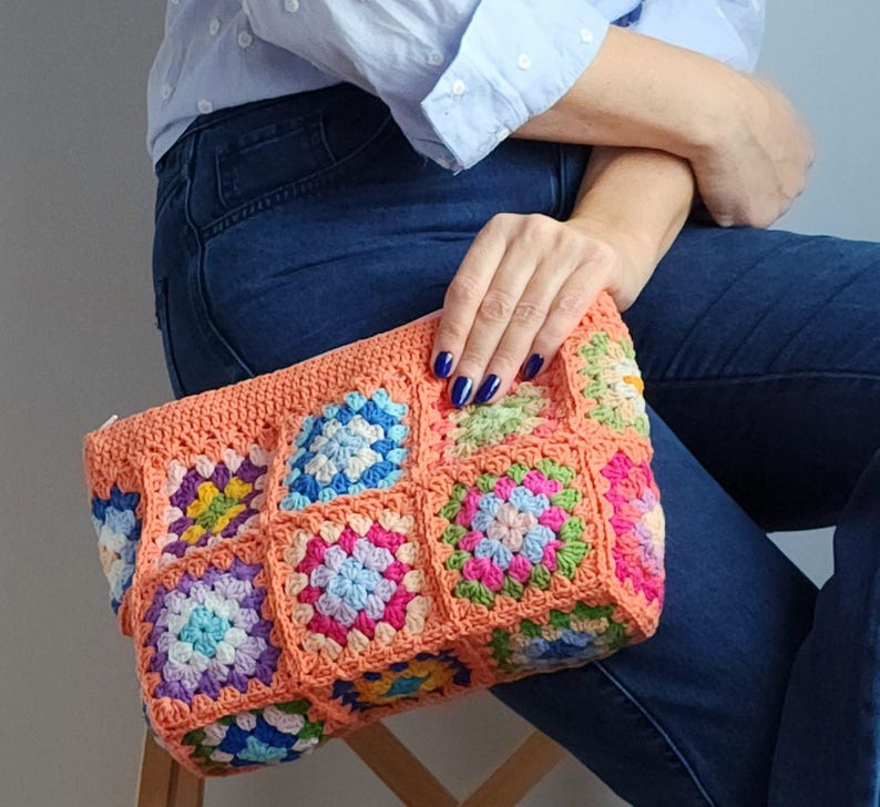 Crochet zipper clutch with peach border and multicolor granny-square panels; handmade crochet purse ideal as a makeup or toiletry bag.