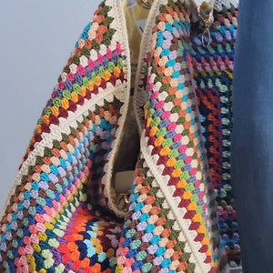 May include: A large, colorful crochet tote bag with black leather handles. The bag is made of a variety of colors, including red, orange, yellow, green, blue, purple, and brown.
