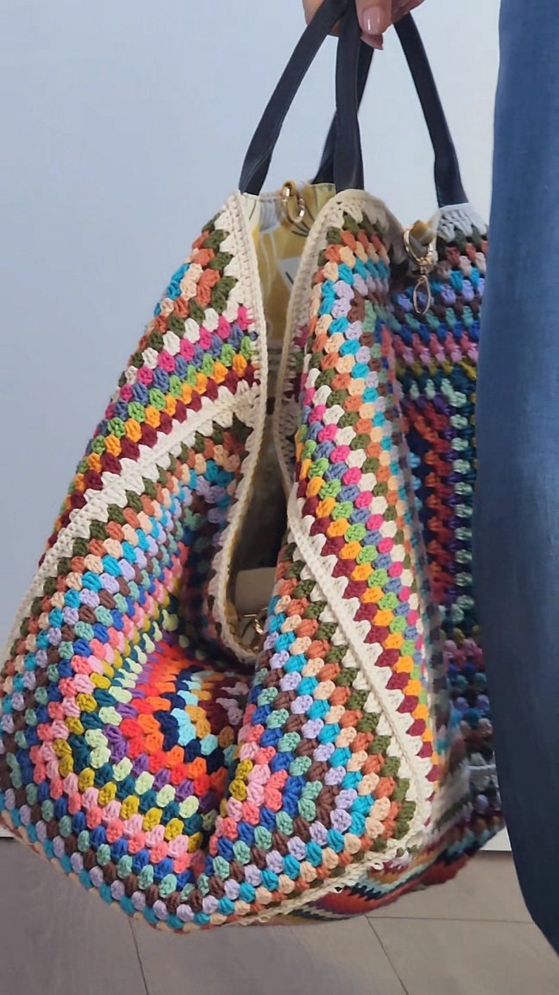 May include: A large, colorful crochet tote bag with black leather handles. The bag is made of a variety of colors, including red, orange, yellow, green, blue, purple, and brown.