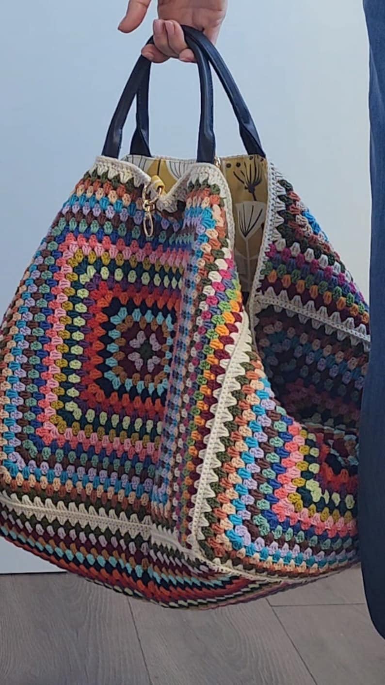 May include: A large, colorful crochet tote bag with black leather handles. The bag is made with a granny square pattern and features a variety of colors, including red, orange, yellow, green, blue, purple, and brown.