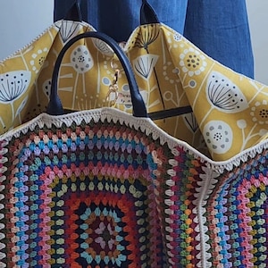 May include: A large, colorful crochet tote bag with a yellow floral fabric lining. The bag has a black leather handle and a zipper closure.