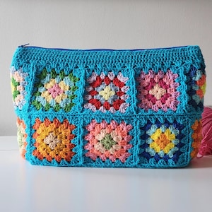 Crochet zipper pouch bag with bright granny-square panels, turquoise edging, and top zipper.