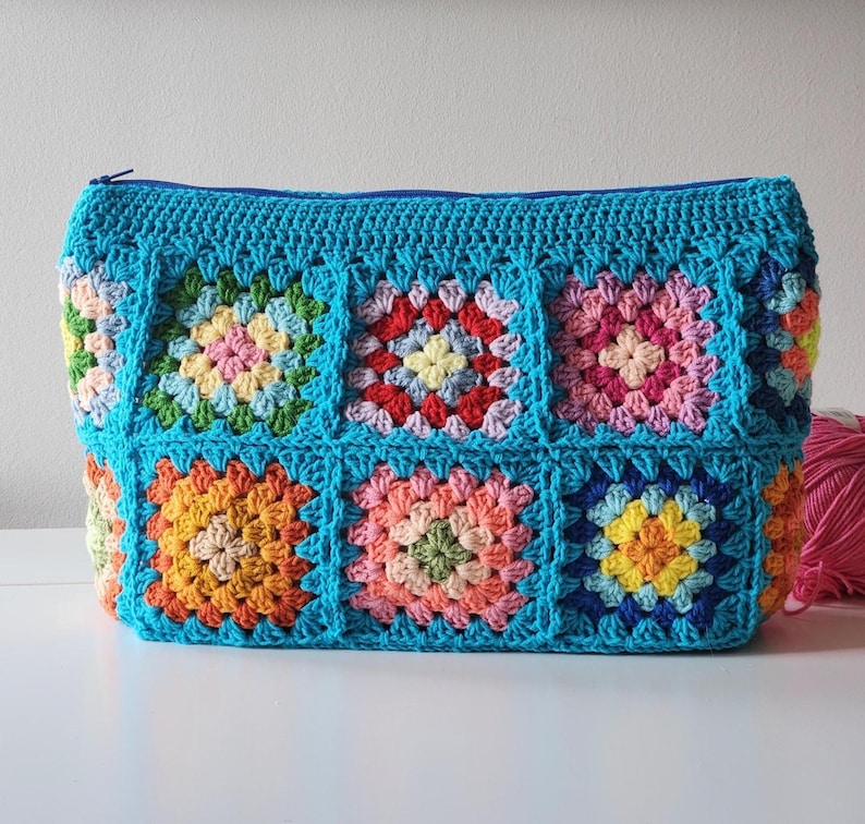 Crochet zipper pouch bag with bright granny-square panels, turquoise edging, and top zipper.