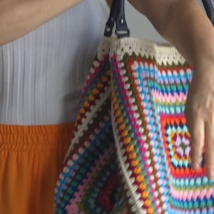 May include: A large, colorful crochet tote bag with a white crocheted trim and black leather handles.