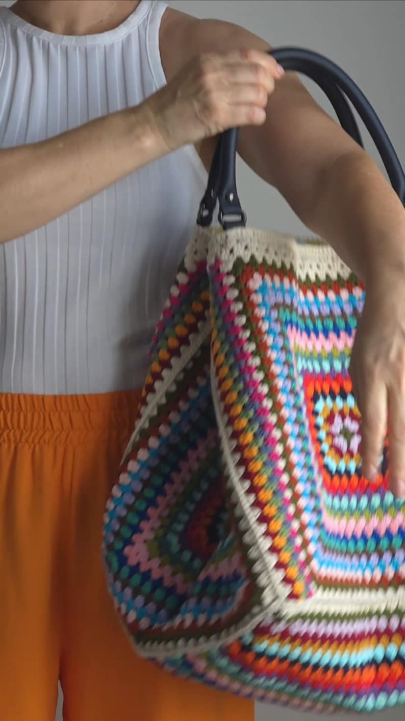 May include: A large, colorful crochet tote bag with a white crocheted trim and black leather handles.
