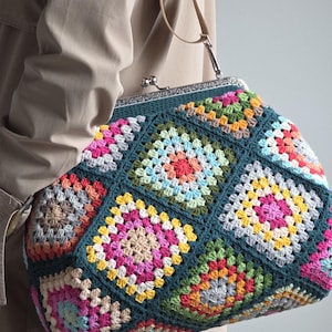 Könnte beinhalten: Handgefertigte Häkeltasche mit teal-farbenem Hintergrund und bunten Quadraten. Die Tasche hat einen Metallverschluss und einen braunen Lederriemen. Die Quadrate sind in Rosa-, Gelb-, Orange- und Grüntönen gehalten. Ein einzigartiges Accessoire.