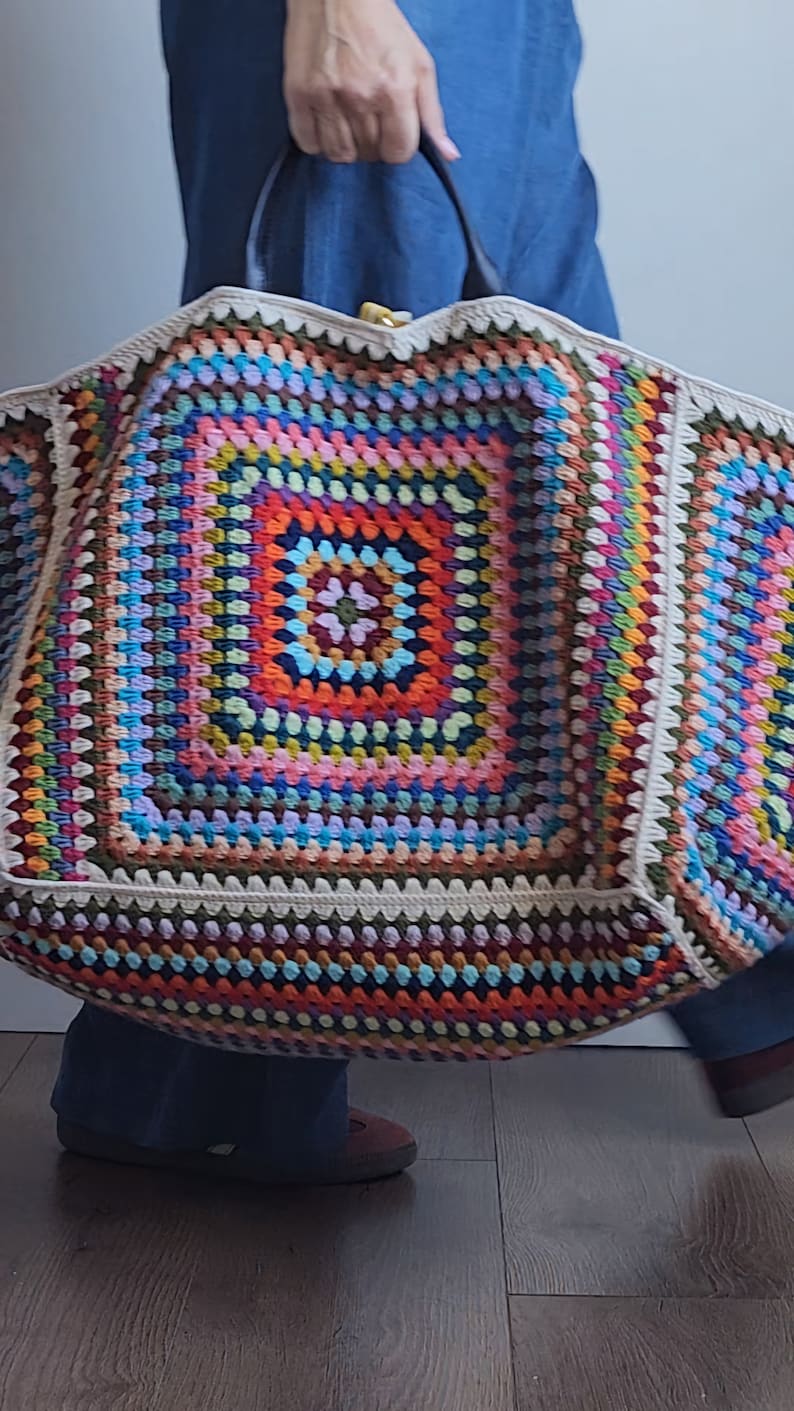 May include: A large, colorful crochet tote bag with a square pattern in the center. The bag is made with a variety of colors, including red, orange, yellow, green, blue, purple, and brown.